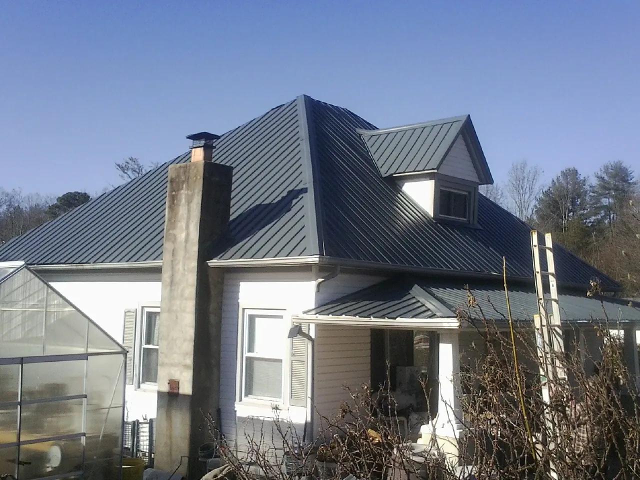 Dark blue standing seam metal roof on a white farmhouse with dormer — Slate & Tile Roof Repair by Roofing Brothers in Carbonado