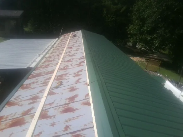 Old rusted panels beside newly installed green metal roofing — Wind Damage Roof Repair by Roofing Brothers in Carbonado