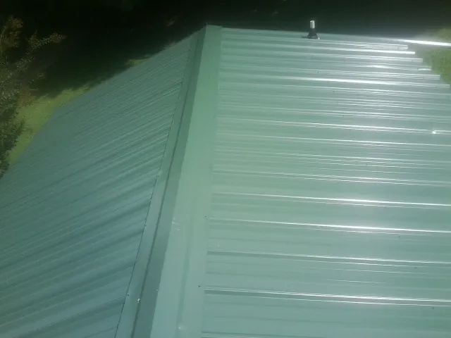 New green metal panels meeting at the ridge of a roof — Flat Roof Repair work by our crew in Carbonado