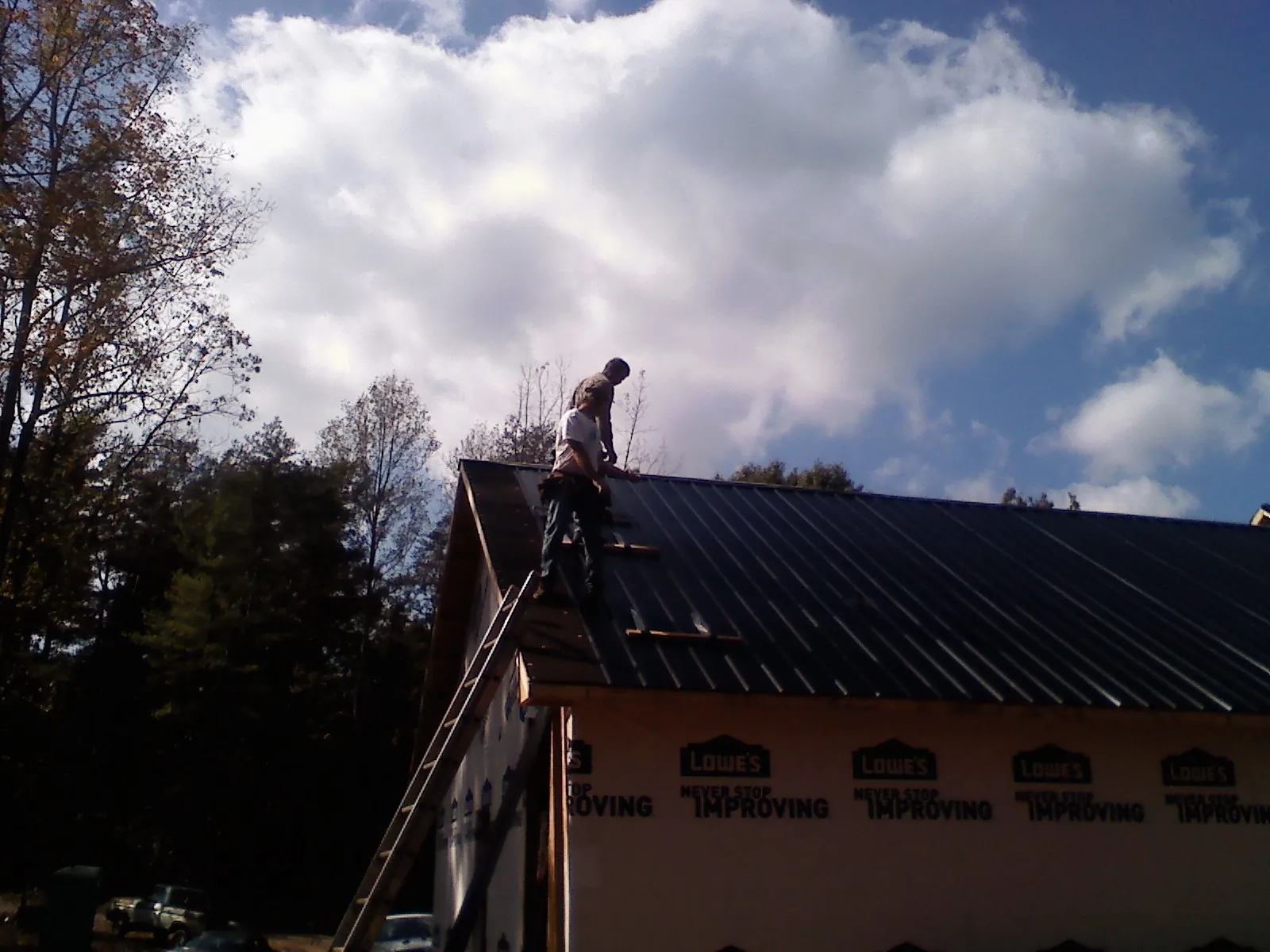 Roofer fastening dark metal panels high against a cloudy sky, from a Roof Inspection job in Carbonado
